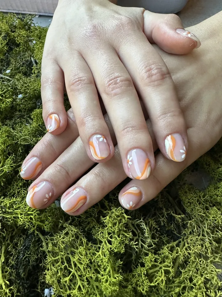 Uñas cortas nude con ondas naranjas y flores blancas